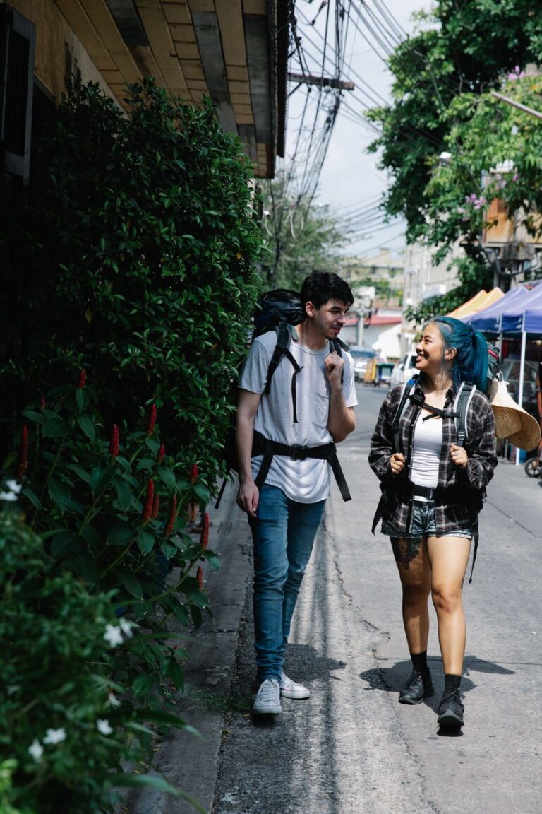 cheerful diverse couple of travellers strolling on narrow street carrying backpacks